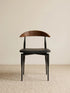 Noren dining chair front view showing curved walnut backrest and black upholstered seat on slender steel legs