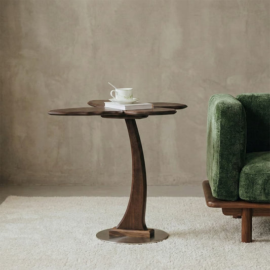 Artistic flower-shaped side table made of solid walnut with a curved organic stem and a metal base, serving as a unique accent piece next to a sofa.