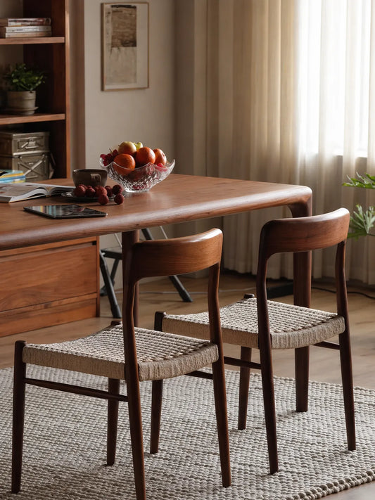Two Orin woven cord walnut dining chairs tucked under a solid walnut dining table in a sunlit room
