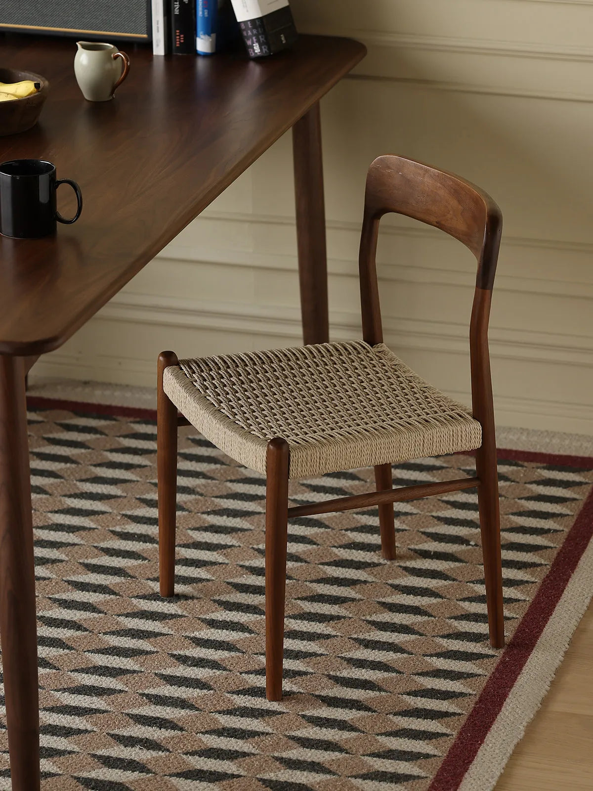 Orin woven cord dining chair viewed from the rear beside a walnut dining table