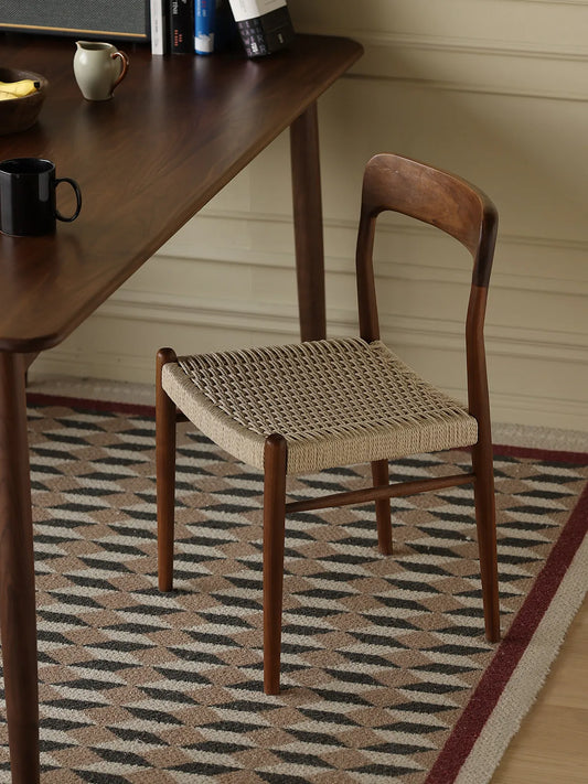 Orin woven cord dining chair viewed from the rear beside a walnut dining table