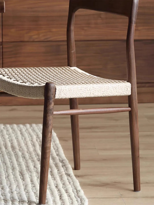Close side view of Orin dining chair walnut frame and paper cord weave against wood-paneled wall