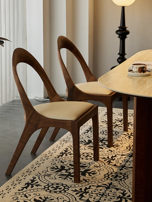 Angled lifestyle shot of two Oryn dining chairs at a walnut table, highlighting the leg structure and natural wood finish.