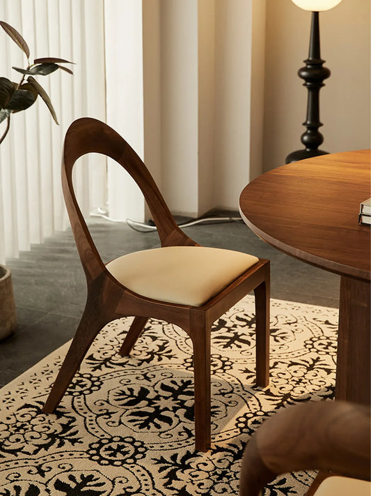 Rear view of the Oryn dining chair showing the sculpted arch and tapered rear legs in solid walnut.