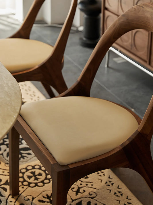 Close-up of the Oryn chair's cream upholstered seat cushion resting on the solid walnut seat frame.