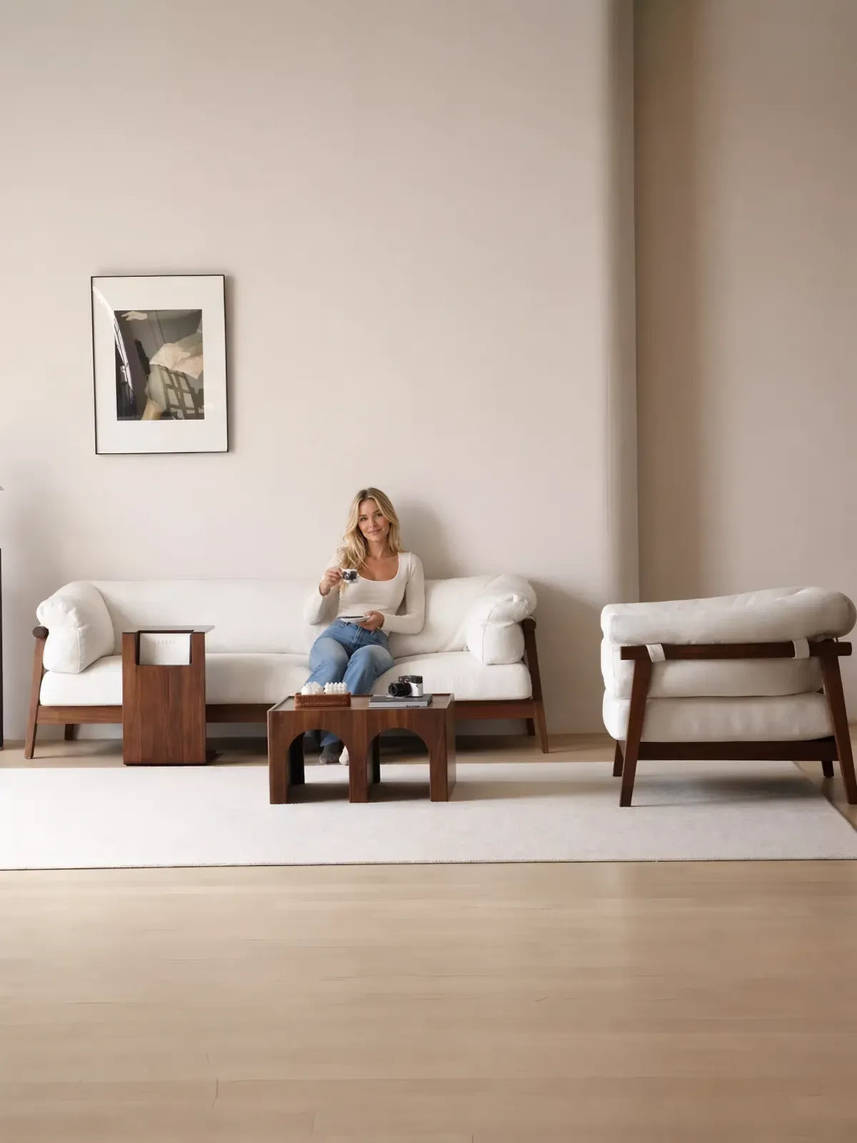 Woman seated on Oslo 3-seater walnut frame sofa with matching accent chair in a minimalist living room