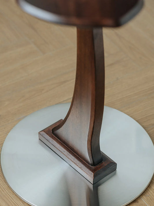Close-up of the Papillon Solid Walnut Accent Table's curved wooden leg and weighted circular metallic base.