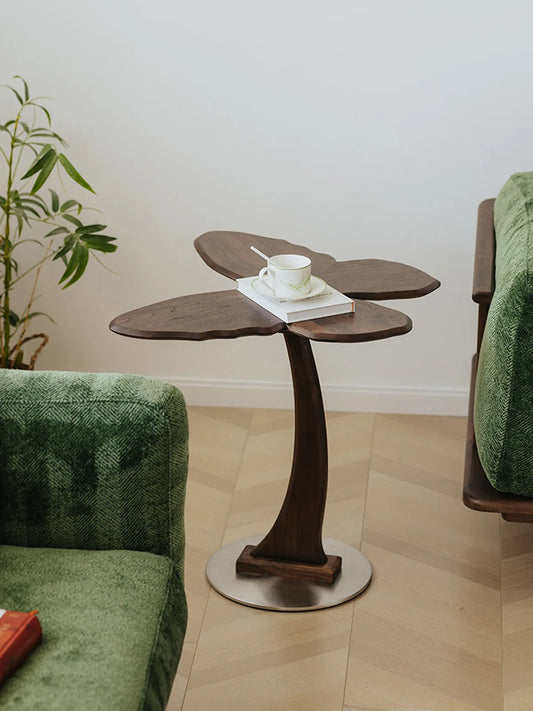 The Papillon Solid Walnut Accent Table styled in a living room next to a green sofa, used as a coffee and book rest.