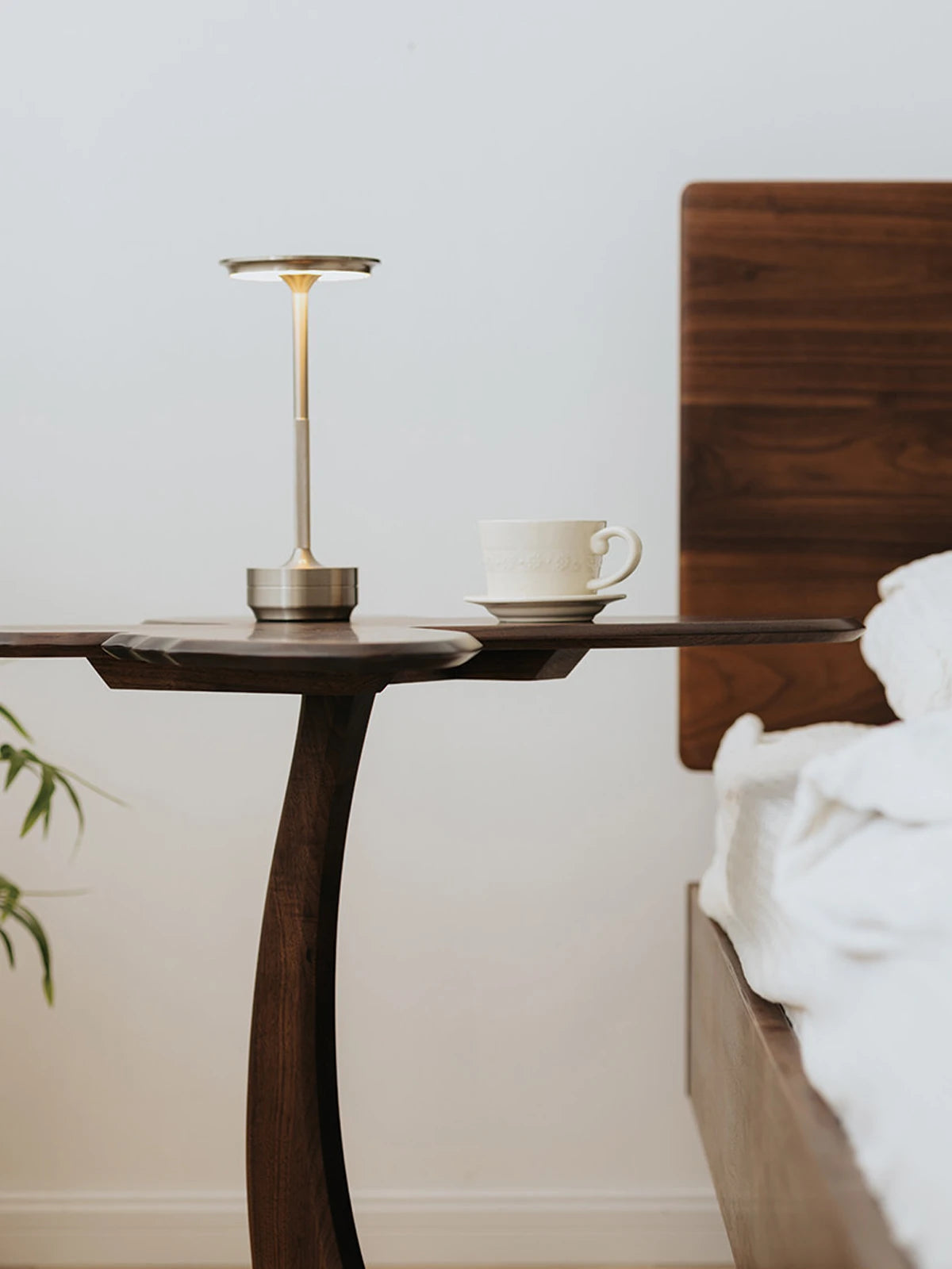 Side profile of the Papillon table showing the elegant, slender curved leg and its functional use as a bedside companion.