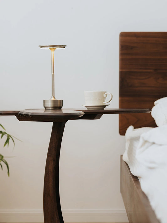Side profile of the Papillon table showing the elegant, slender curved leg and its functional use as a bedside companion.