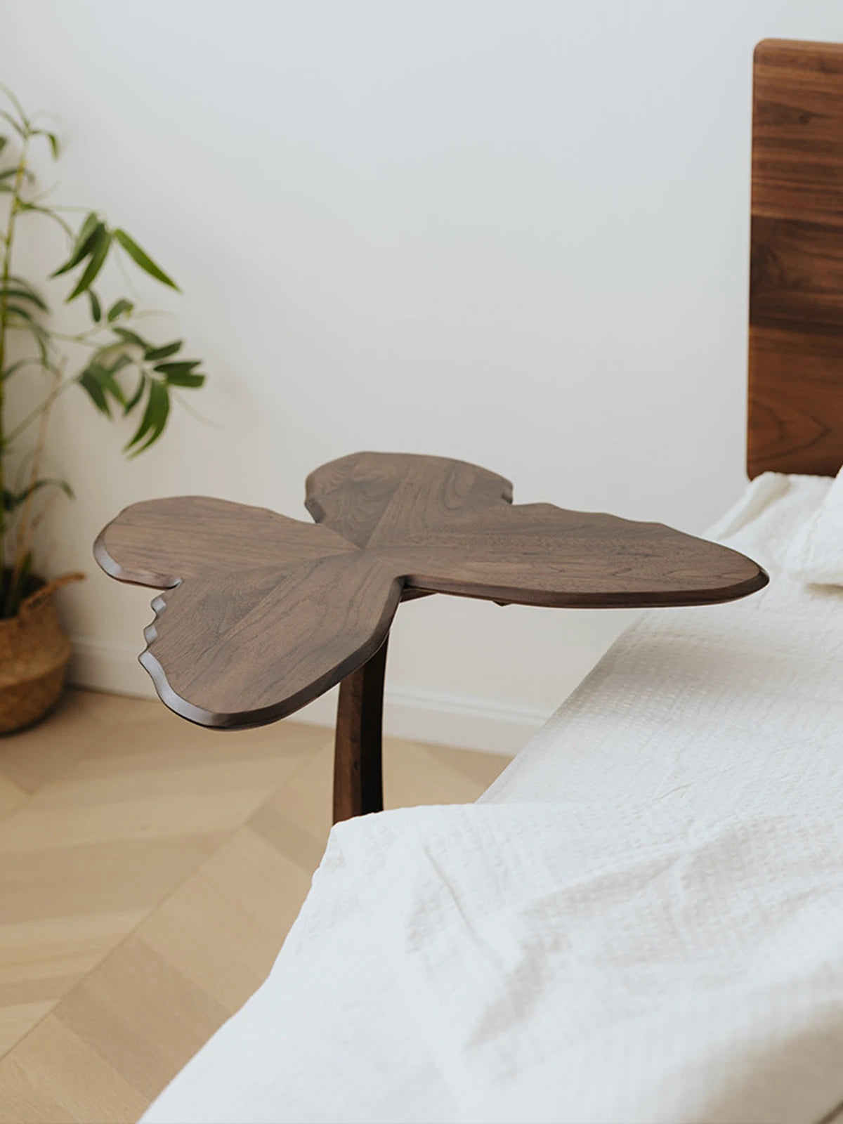 The Papillon walnut accent table utilized as a unique bedside table, highlighting its butterfly-shaped silhouette.