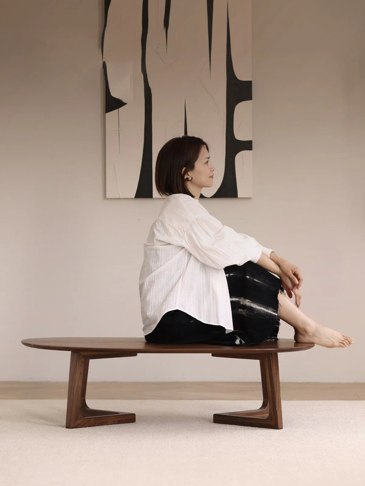A woman sitting on the large Pebble Coffee Table, demonstrating the sturdy and reliable construction of the solid walnut base.
