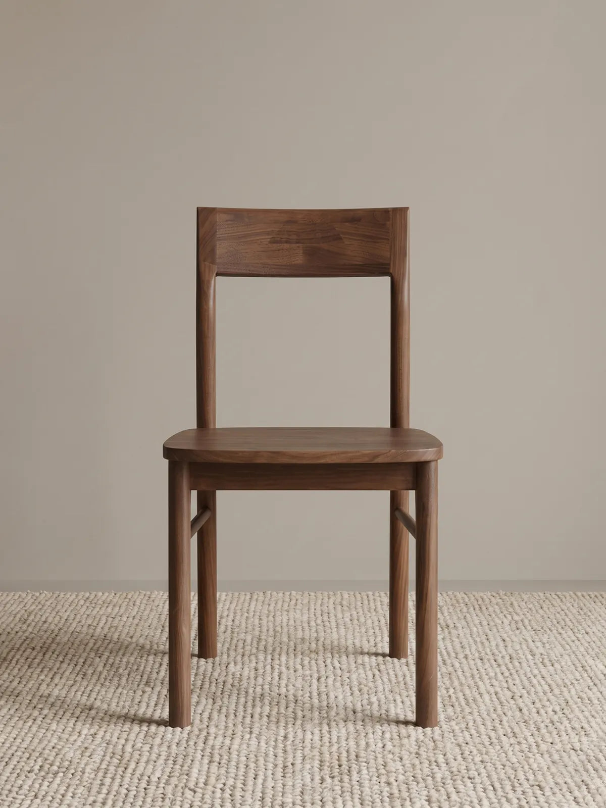 Riven solid walnut dining chair seen from the front, showing low curved backrest, contoured wood seat, and rounded stretcher bars