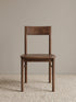 Riven solid walnut dining chair seen from the front, showing low curved backrest, contoured wood seat, and rounded stretcher bars