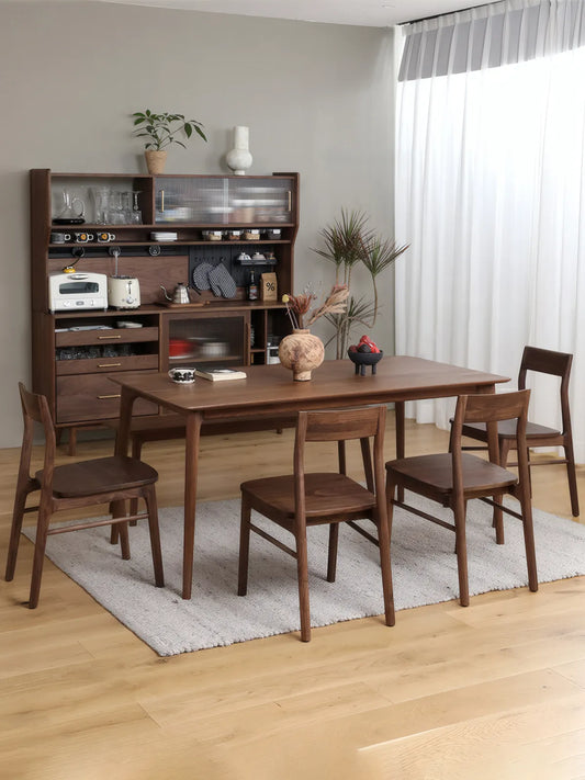 Wide dining room scene with four Riven solid walnut dining chairs around a walnut table, sideboard and sheer curtains in background