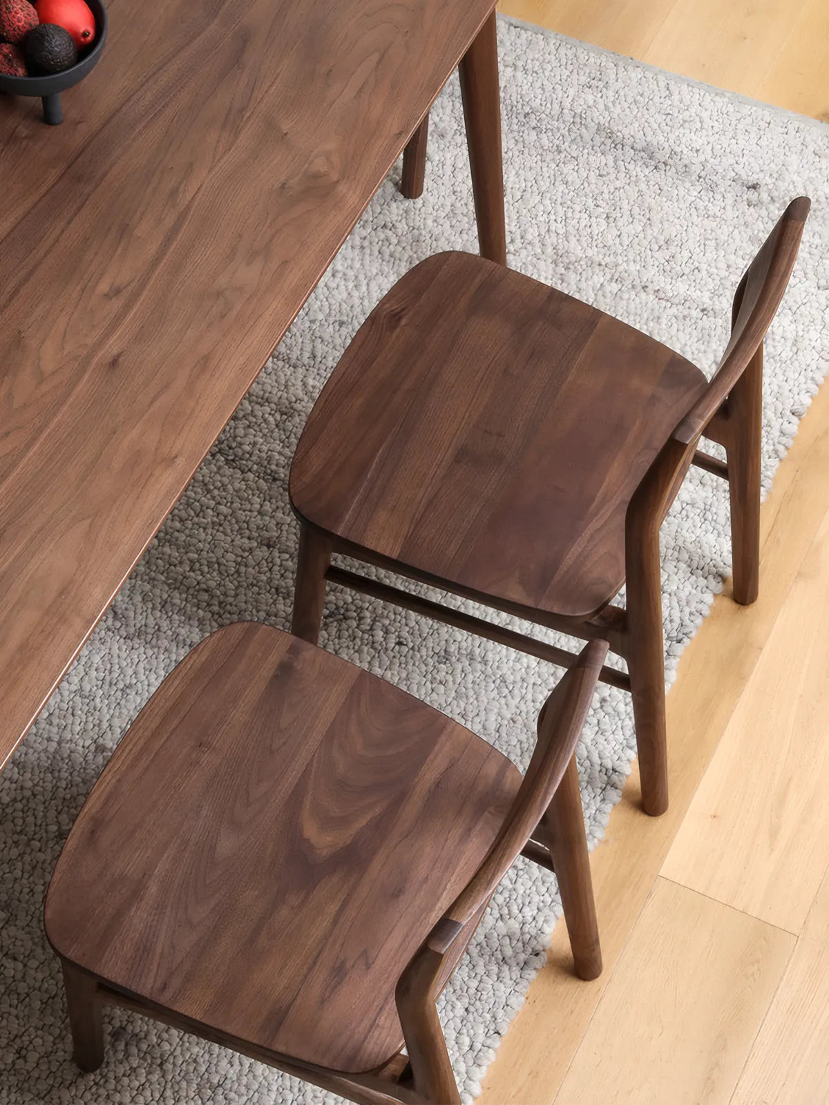 Overhead view of two Riven walnut dining chairs tucked under a walnut dining table, showing broad wood seat grain and open backrest