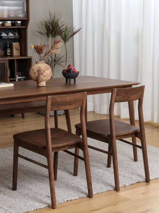 Two Riven solid walnut dining chairs at a walnut dining table in a styled dining room with sideboard and plants