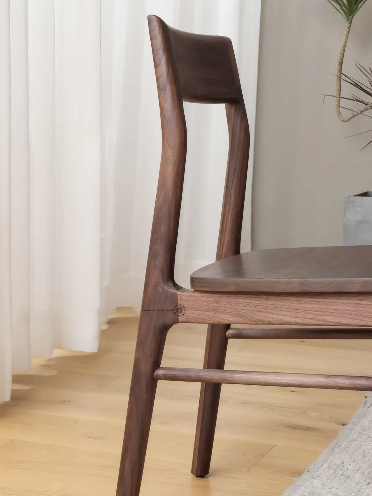 Close-up side view of the Riven dining chair showing sculptural back leg, joinery at the seat junction, and walnut grain detail