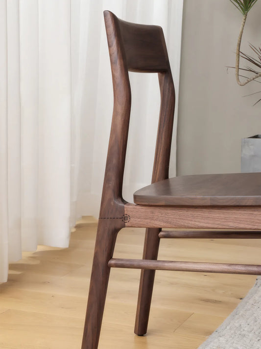 Close-up side view of the Riven dining chair showing sculptural back leg, joinery at the seat junction, and walnut grain detail
