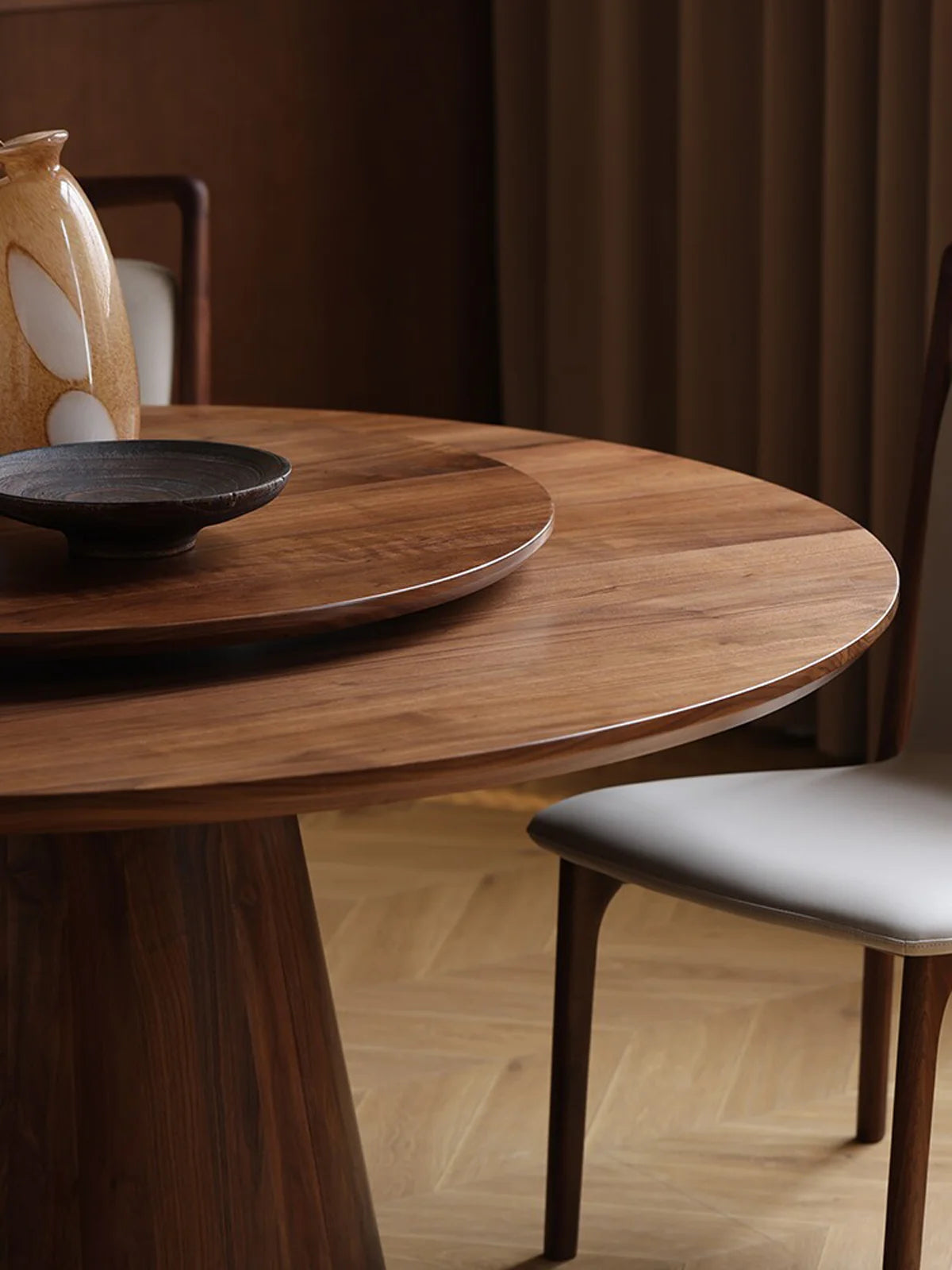 Close-up of the dark walnut round dining table highlighting the wood grain, built-in lazy Susan, and adjacent dining chair.