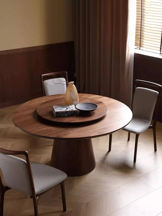 Dark walnut round dining table styled in a dining room with light upholstered chairs and a central lazy Susan, creating a warm modern look.