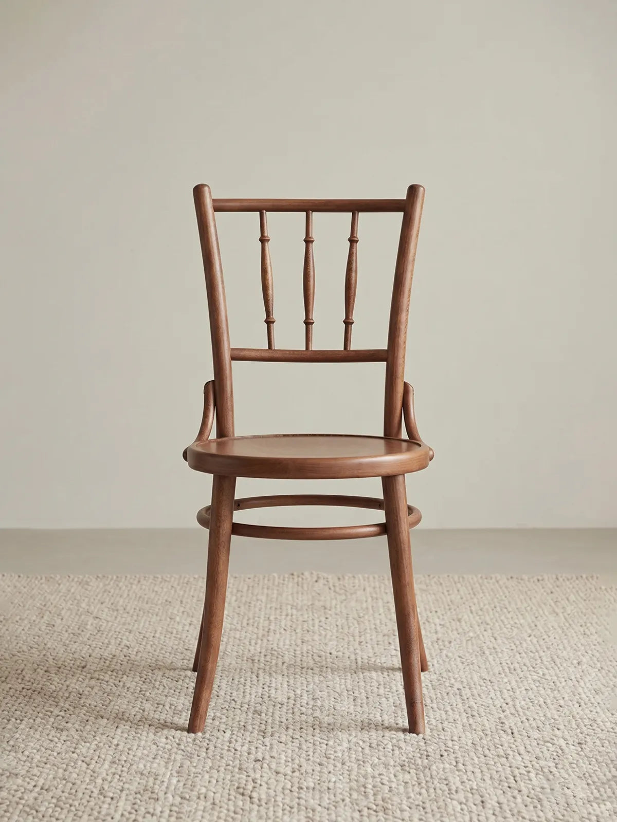 Salo spindle back dining chair in solid walnut, front view showing turned bobbin spindles, round seat, and splayed legs on a neutral rug