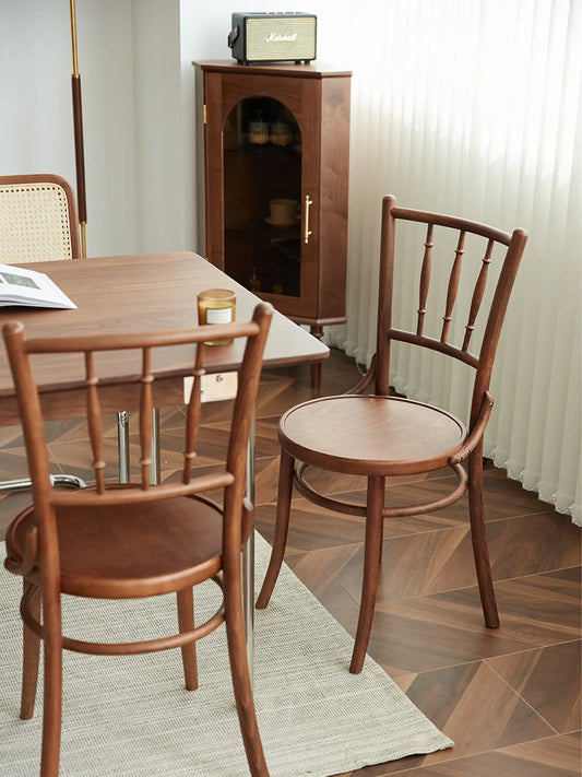 Two Salo spindle back walnut dining chairs at a dining table in a styled living space with cabinet and herringbone floor
