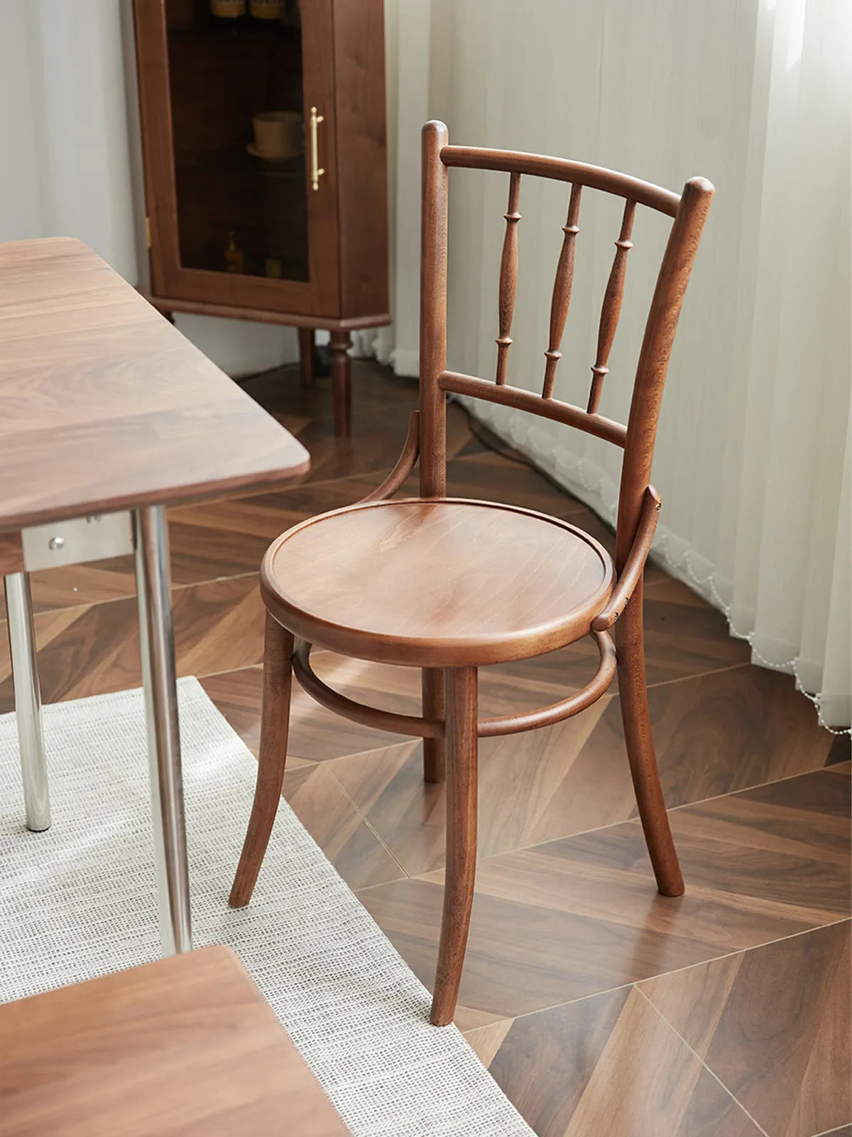 Salo walnut dining chair seen from the rear three-quarter angle beside a dining table on herringbone wood flooring