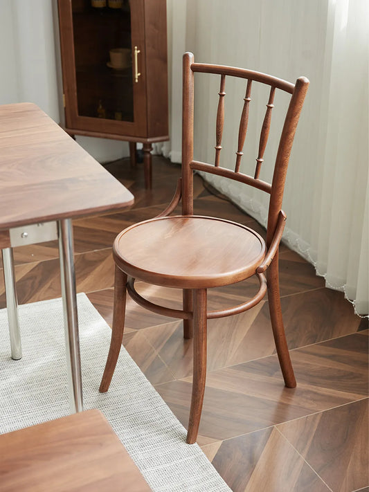 Salo walnut dining chair seen from the rear three-quarter angle beside a dining table on herringbone wood flooring