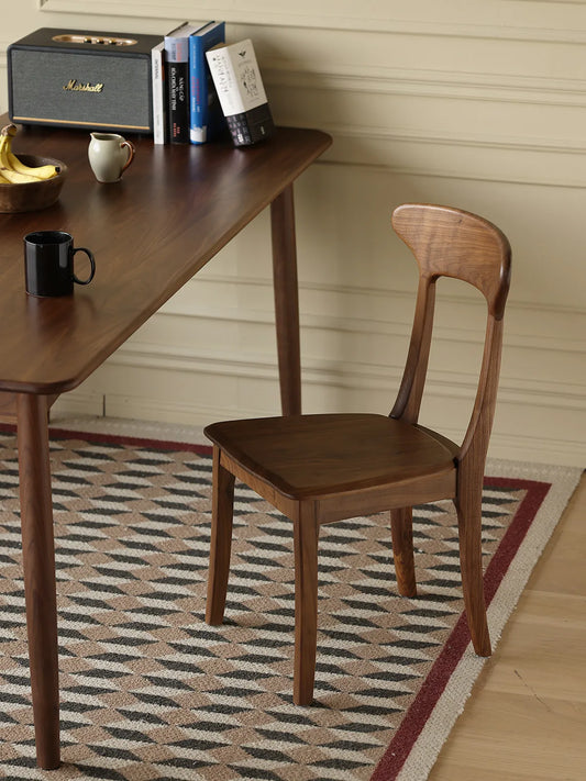 Sora dining chair in solid walnut tucked beside a walnut dining table in a styled room with books and a Marshall speaker