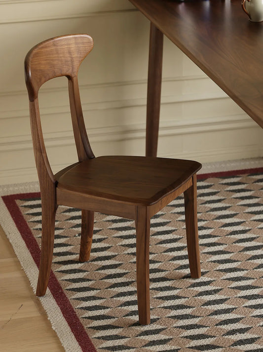 Sora walnut dining chair from a rear three-quarter angle beside a dining table on a patterned rug