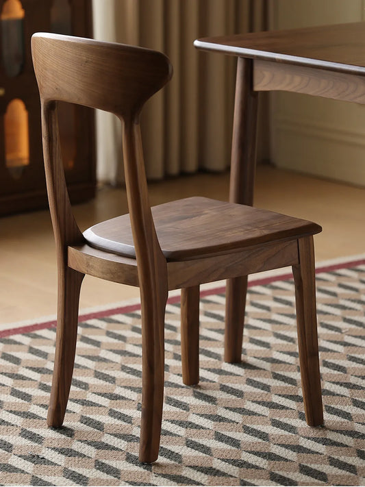 Rear view of the Sora walnut dining chair showing the sculpted back, tapered legs, and warm wood tones beside a dining table