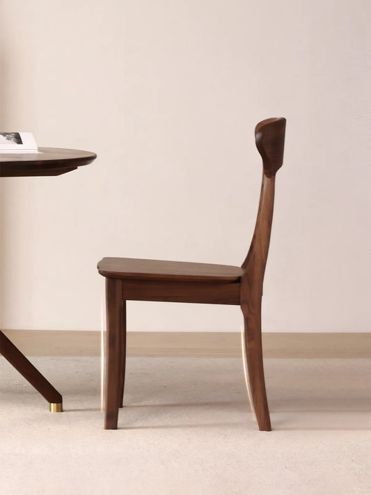 Side profile of the Sora dining chair in solid walnut showing the continuous rear leg and curved backrest silhouette