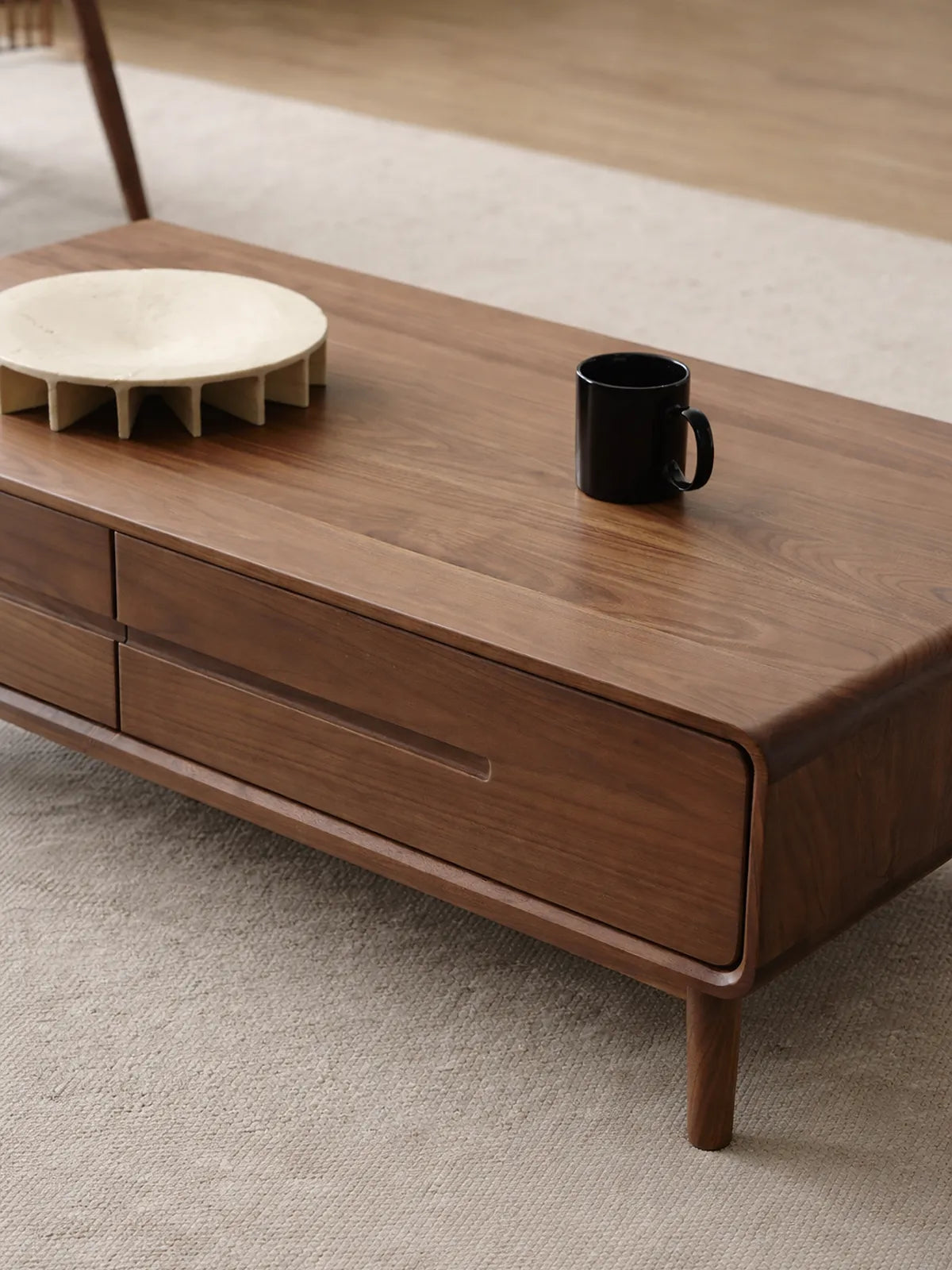 Close-up of a solid walnut coffee table with rounded corners, integrated drawer front, and softly finished top surface
