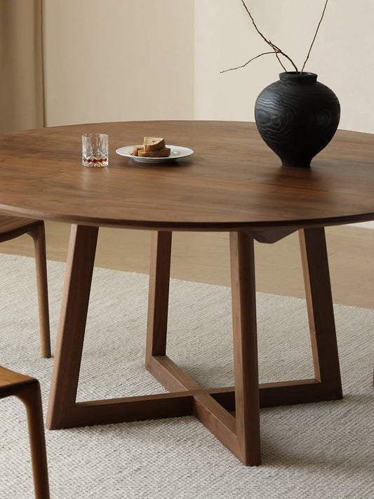 Close view of the trestle pedestal base and rich walnut grain on a round dining table with a softly beveled top.