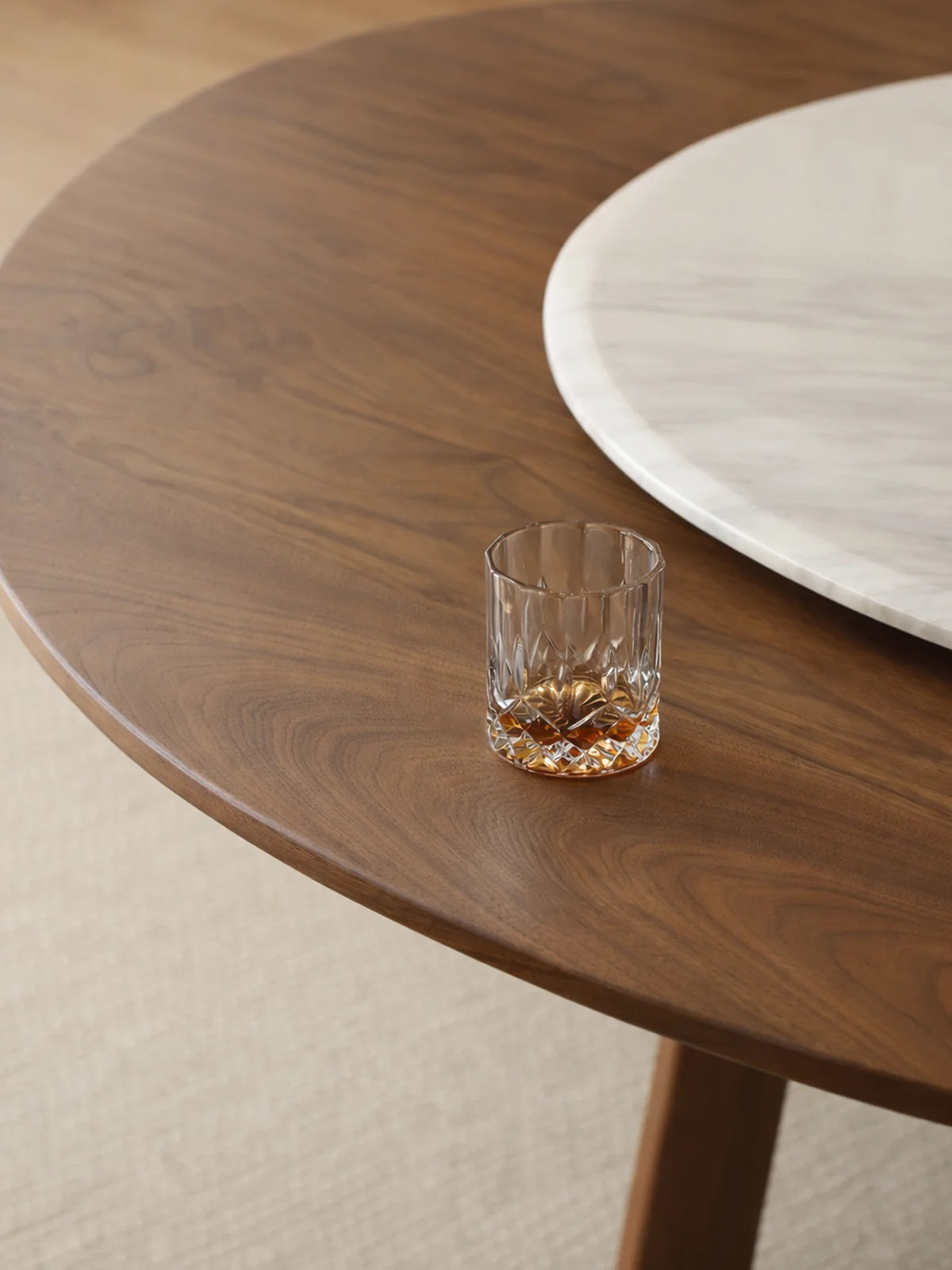 Close-up of the walnut tabletop grain and beveled edge beside a white marble lazy Susan and a glass on the table surface.