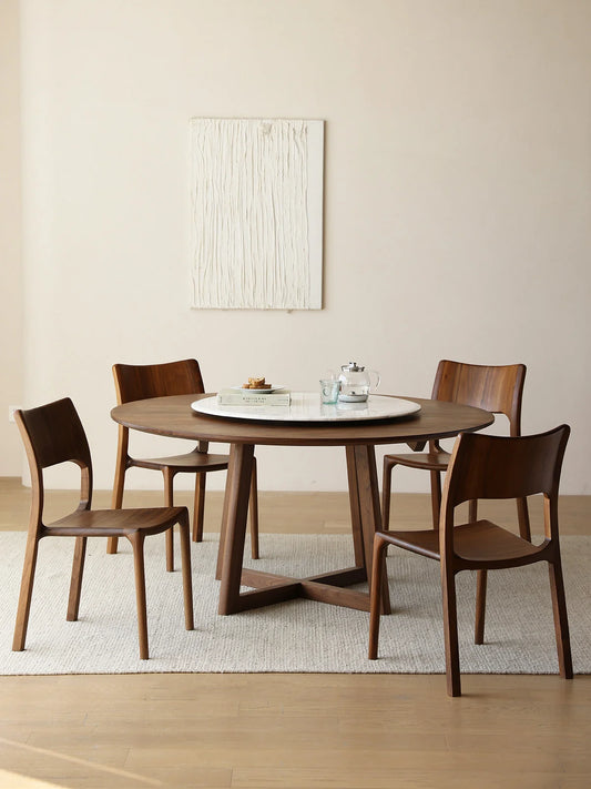Front view of a round walnut dining table with four matching chairs and a white marble lazy Susan in a bright, pared-back interior.