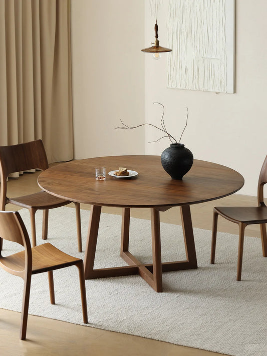 Round American black walnut dining table with sculptural trestle base, styled with four walnut chairs in a calm neutral dining room.