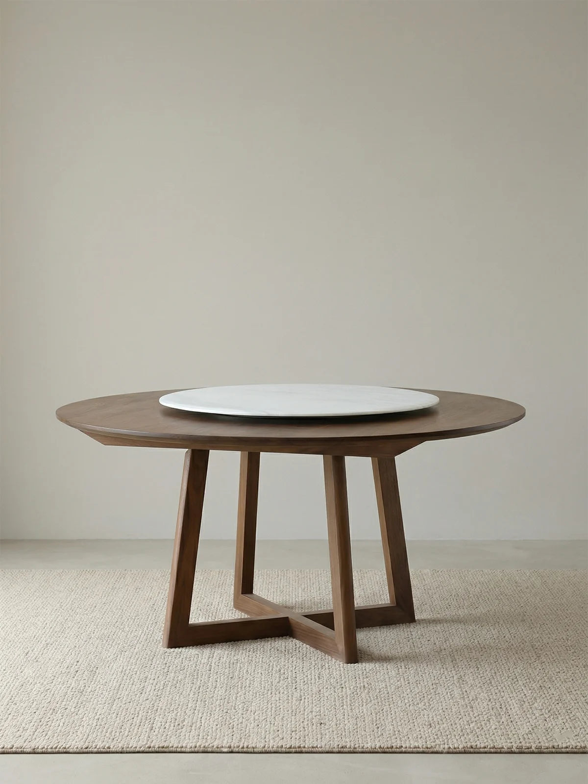 Isolated view of a round walnut dining table with trestle base and centered white marble lazy Susan on a woven rug.