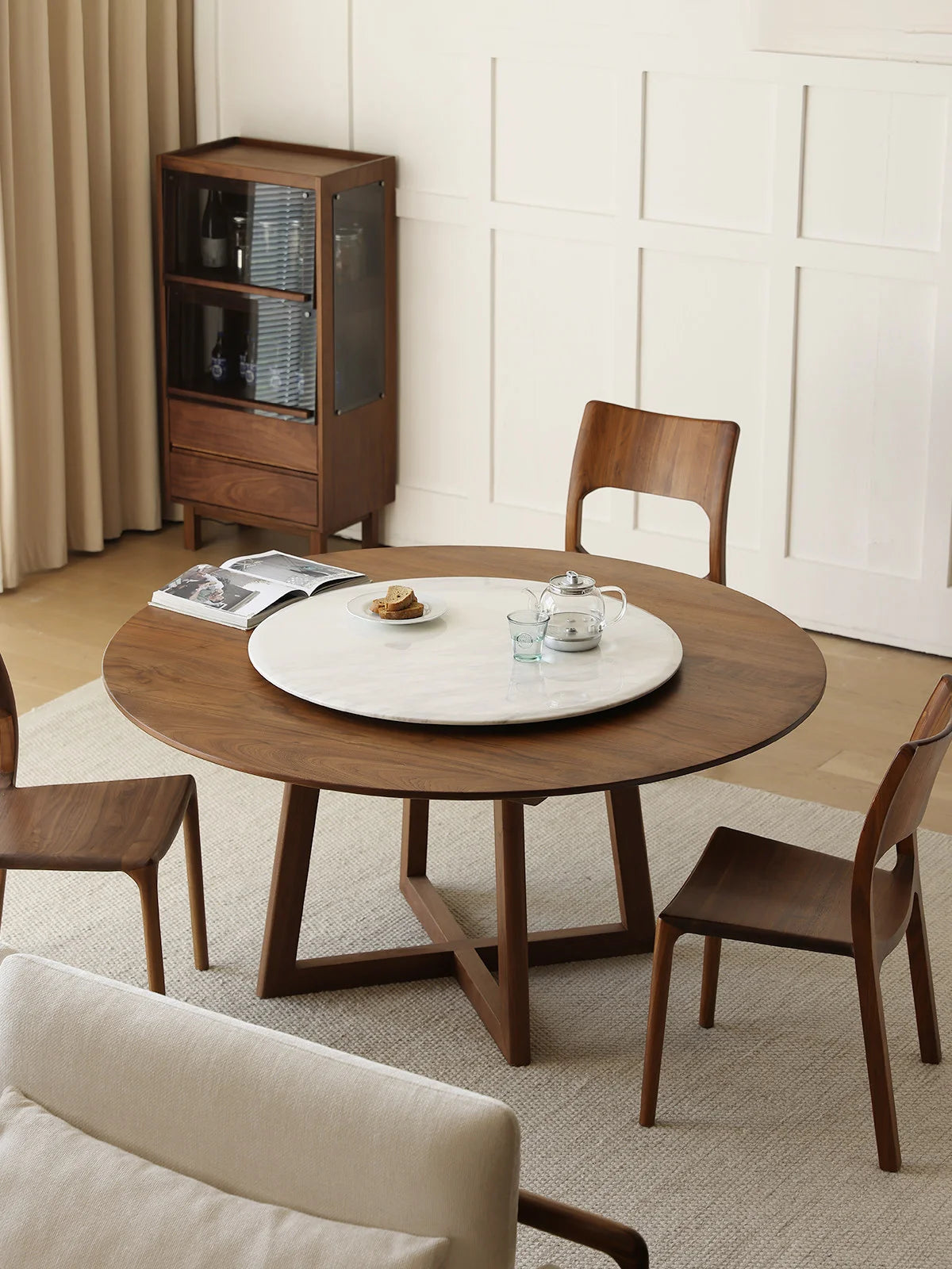 Overhead room view of a round walnut dining table with marble lazy Susan, walnut chairs, and minimalist dining room styling.