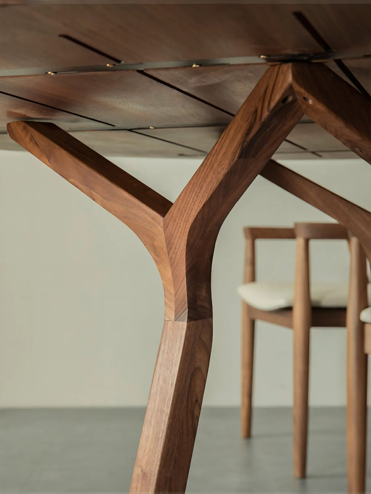 Close-up of the walnut dining table base showing sculpted legs, underside support structure, and circular stretcher detail.