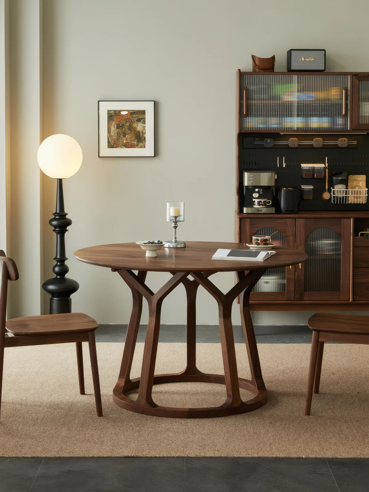 Front view of a round solid walnut dining table with an open sculptural base, styled in a warm modern interior.