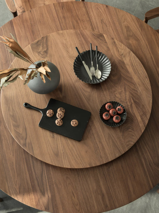 Top view of the round walnut dining table with a central lazy susan, highlighting the circular form and expressive walnut grain.