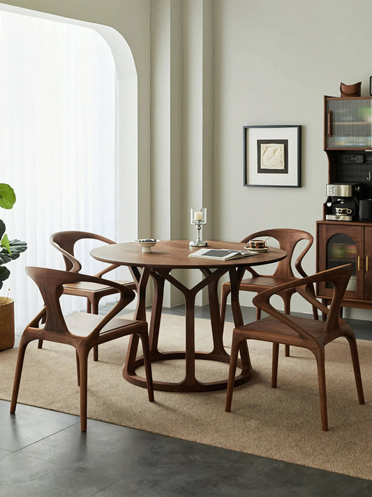 Angled lifestyle view of a round walnut dining table for four with a sculptural base in a softly lit modern dining room.