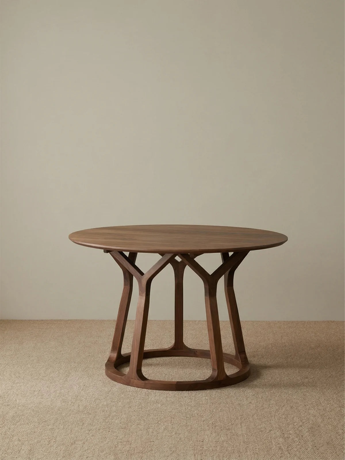 Studio view of a round solid walnut dining table with integrated lazy susan and an open sculptural pedestal base.