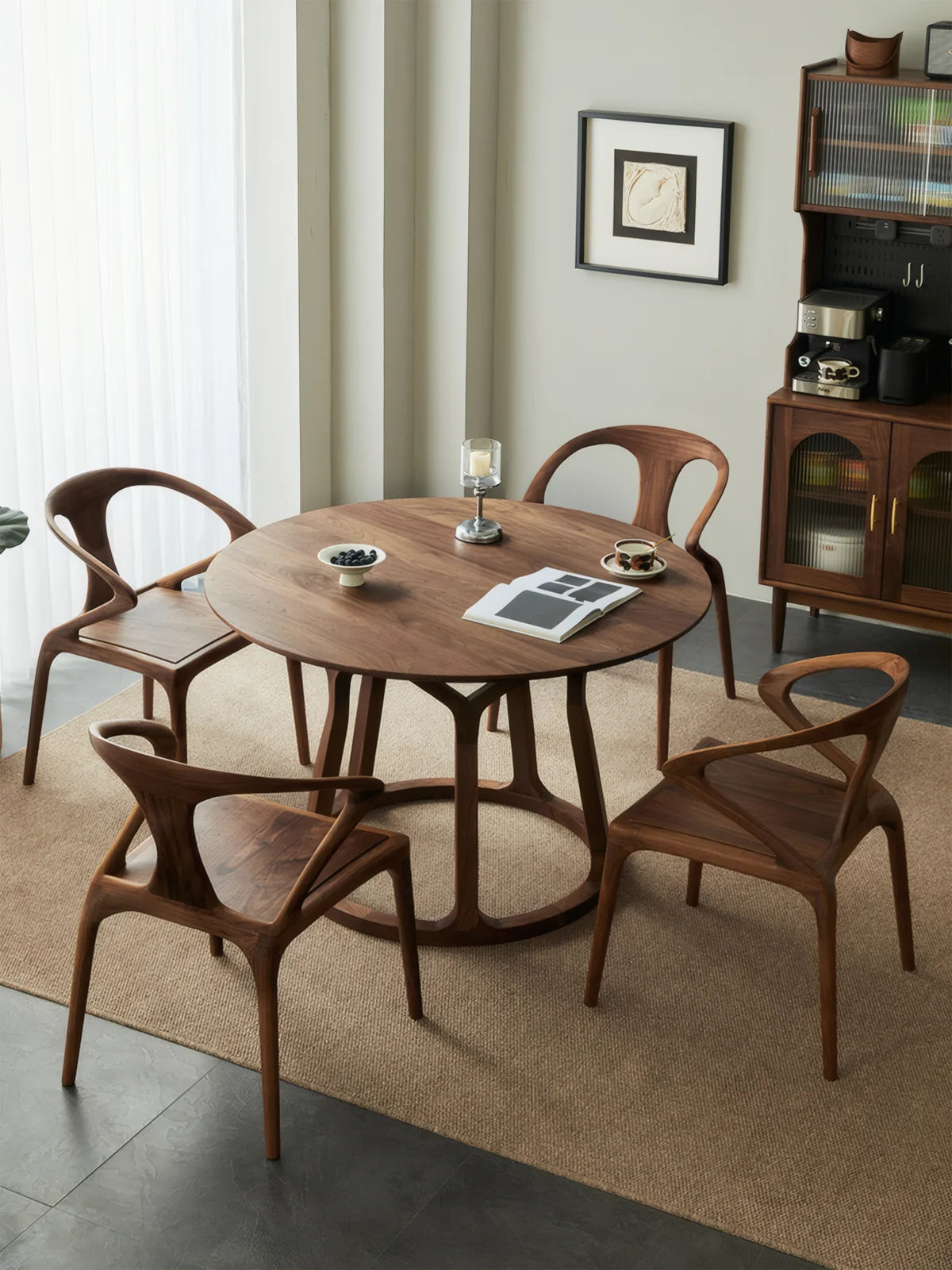 Round solid walnut dining table with four sculptural chairs in a minimalist dining room, shown with an airy pedestal base and warm natural grain.