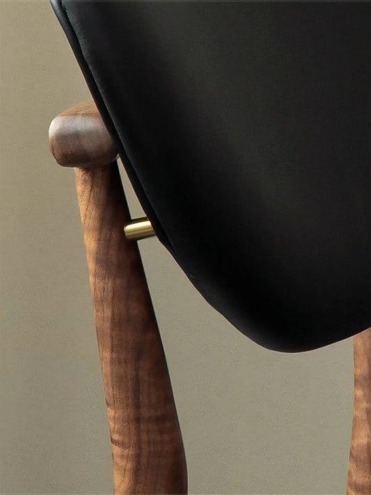 Close-up macro shot of the antique brass spacer on the Sylvan modern walnut dining chairs, showing rich North American wood grain texture.
