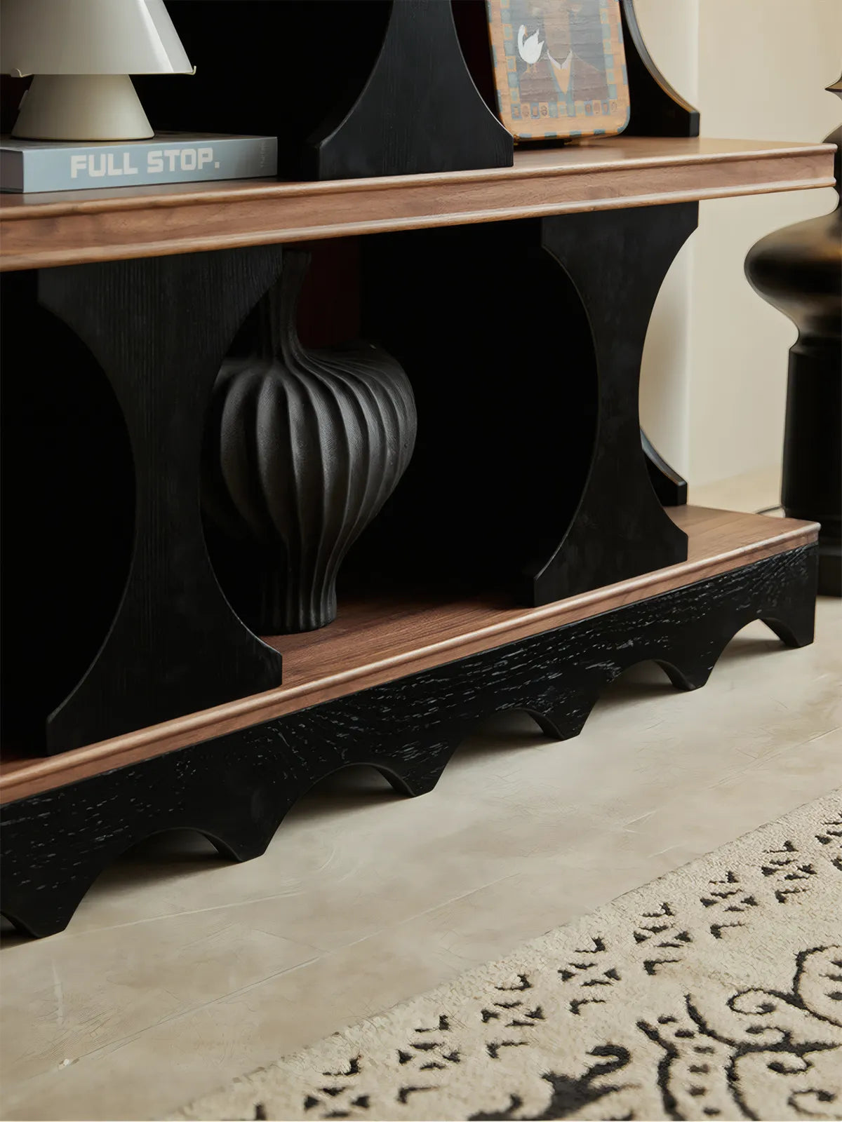 Close-up macro shot of the rich North American black wood grain on the curved base of the Sylvan solid walnut bookshelf.