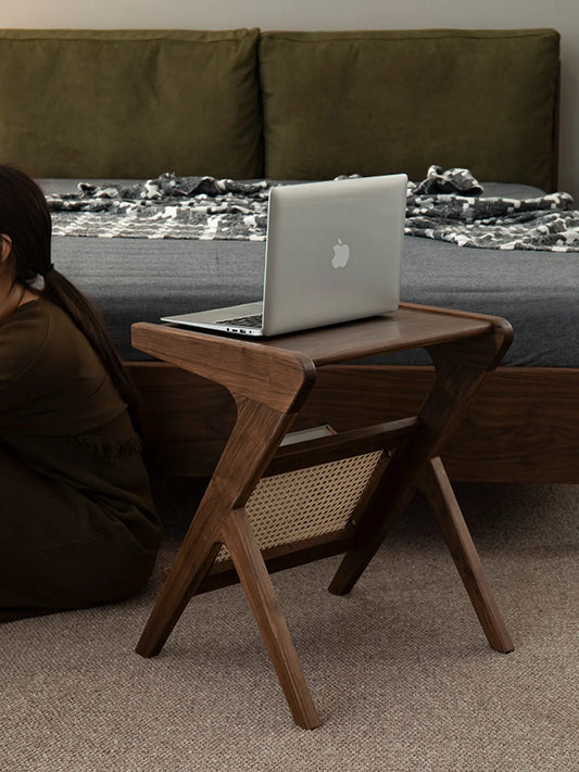 Rear view of the Sylvan walnut table placed next to a bed, demonstrating its use as a compact nightstand.