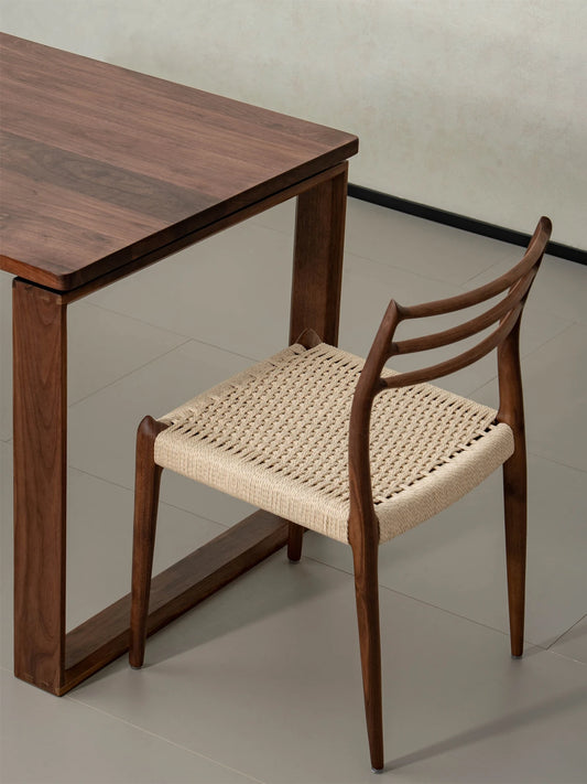 Angled top-down view of The Haven Dining Chair with a woven paper cord seat, beautifully paired with a matching solid Black Walnut dining table.
